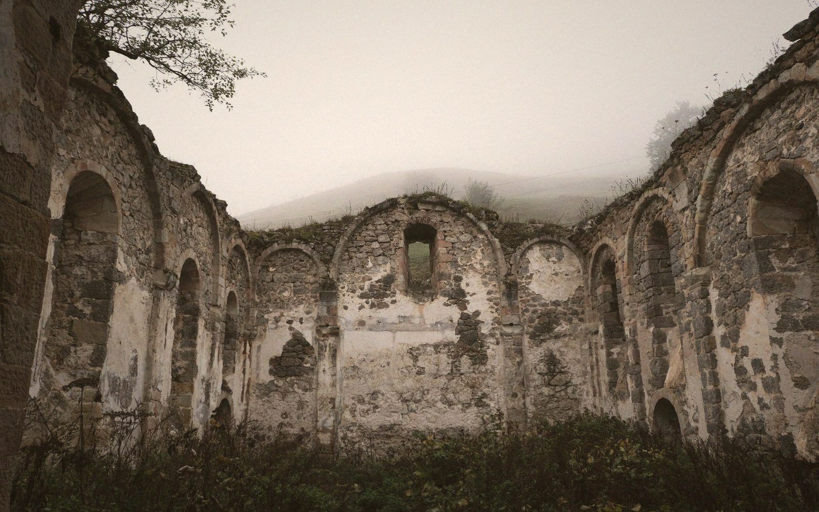 Roofless stone ruin with arched alcoves stands open to foggy sky and hills