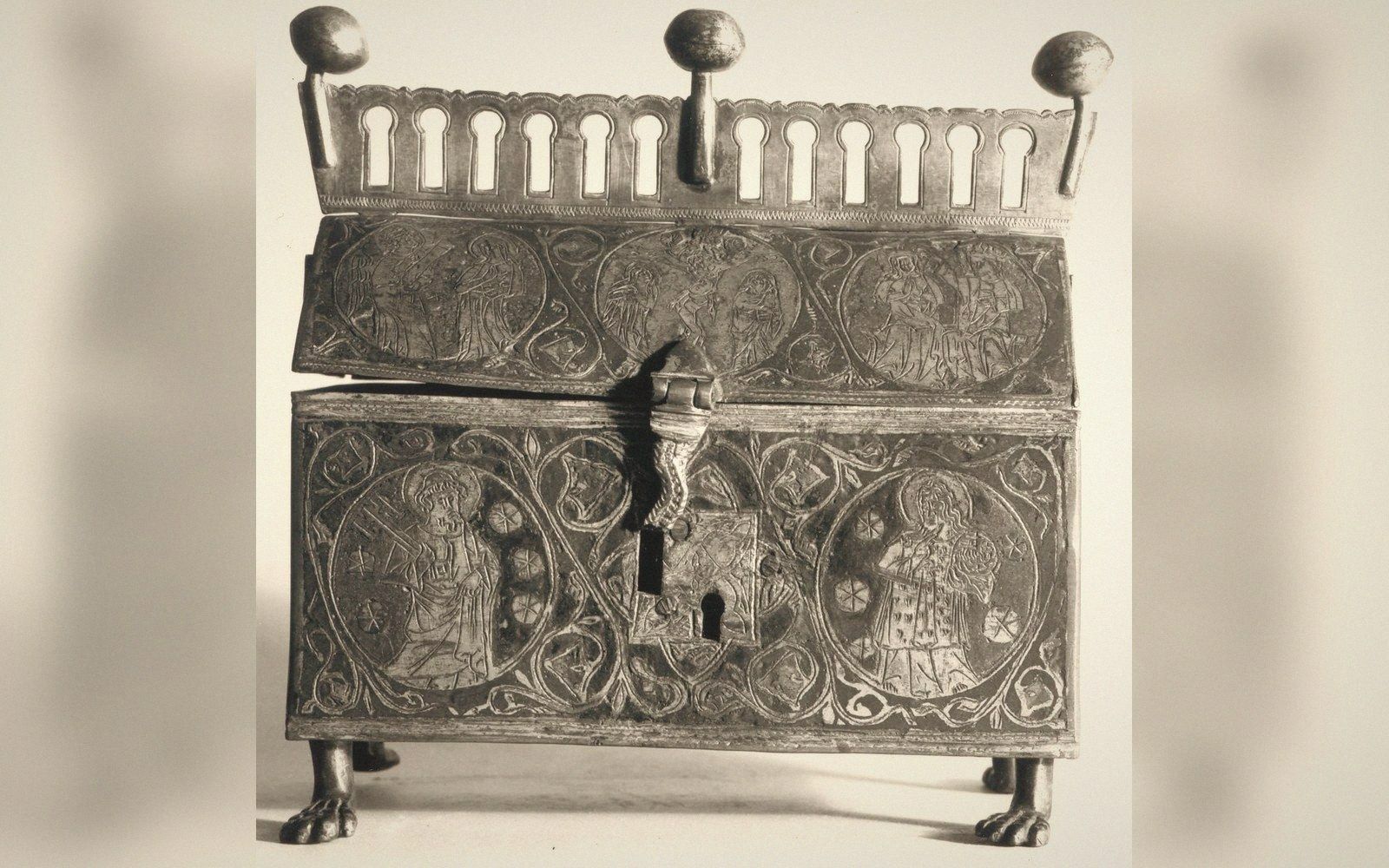 A house-shaped metal reliquary on a plain dark ground